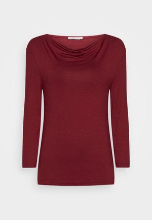 Haut pour femme bordeaux à manches longues avec un col drapé et une silhouette ajustée sur un fond blanc uni.