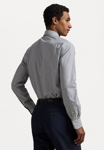 Camisa de mangas largas para hombre en un patrón de cuadros en blanco y azul marino, con cuello alzado y puños abotonados, combinada con pantalones oscuros.