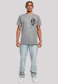 Grå bomullströja med rund halsringning som har en svart grafisk design, inklusive logotyper och text. Matchad med ljusblå jeans och vita sneakers.