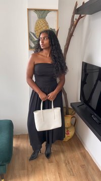 Μαύρο strapless φόρεμα με ραμμένο σώμα, μακριά φούστα, συνδυασμένο με μαύρες μυτερές γόβες και μια λευκή τσάντα. Φυσικό φως με ξύλινο πάτωμα.