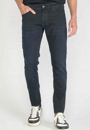 Jean slim-fit bleu foncé en denim, avec cinq poches, fermeture à bouton et détails de couture subtils le long des coutures.