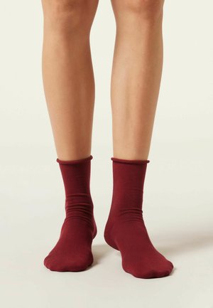 Chaussettes de cheville bordeaux en tissu doux et extensible, offrant un ajustement serré avec un revers roulé en haut. Texture lisse et design sans coutures.