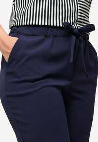 Námořnické modré kalhoty s hladkou texturou, vybavené elastickým pasem a mašlí. Obsahují boční kapsy pro užitečnost.