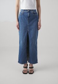 Denimskjørt med en frontsplitt, blå farge, midt på leggen lengde, fem-lommedesign, og en tettsittende midje. Kombinert med svarte hælsandaler.