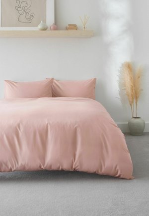 Letto con piumino rosa cipria e cuscini contro parete bianca, mensola sospesa con decorazioni, arte astratta a linee e erba pampas in vaso grigio.