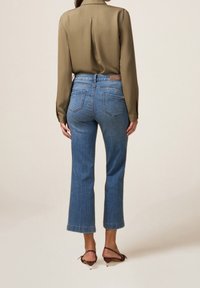 Blusa de manga larga en verde oliva, metida por dentro de unos jeans rectos de tiro alto, de color azul claro, con dobladillo sin rematar y bolsillos traseros. Etiqueta de cuero marrón visible.