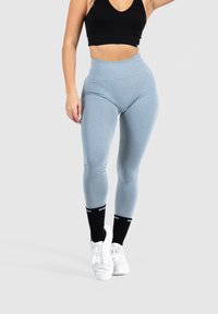 Leggings azul claro con una cintura alta, hechos de un material elástico, combinados con zapatillas blancas y calcetas negras hasta la rodilla con texto.