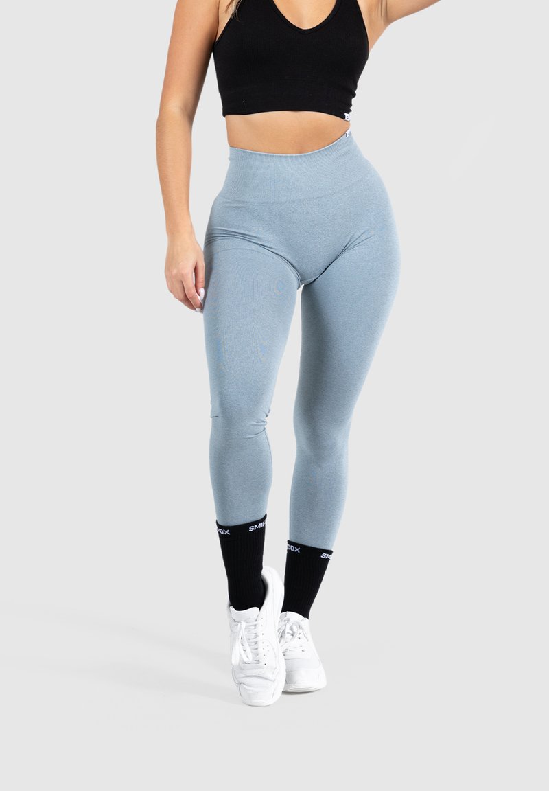 Leggings azul claro con una cintura alta, hechos de un material elástico, combinados con zapatillas blancas y calcetas negras hasta la rodilla con texto.