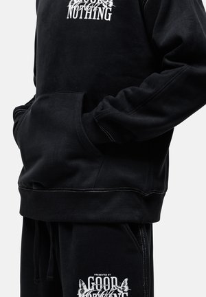 Czarny polarowy hoodie z białym graficznym napisem, posiadający kieszeń i ściągacze na rękawach. W zestawie z czarnymi spodniami z białym logo.