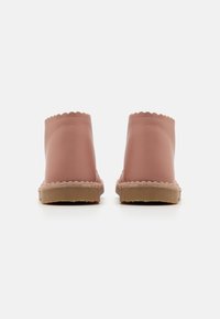 Botas de tobillo de goma rosa con bordes ondulados, un exterior texturizado y una suela marrón clara con un detalle de costura elevada.
