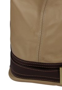 Beige leren tas met een donkerbruine accentband. Heeft zichtbare stiksels en een metalen gespsdetail aan de riem. Gladde textuur.