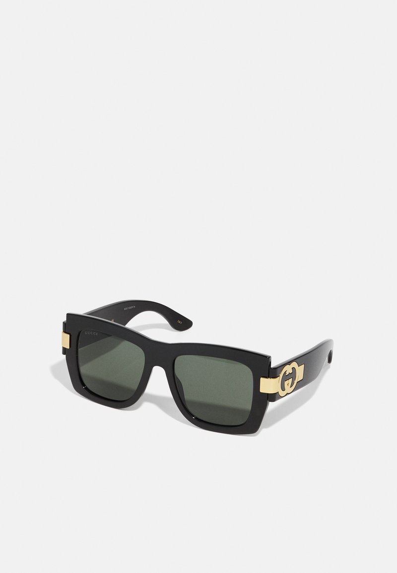 Gafas de sol cuadradas negras con lentes tintados en verde, detalles de herrajes dorados y un logotipo en las ramas. Acabado mate elegante.