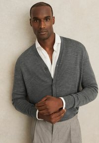 Gray knitted cardigan with a V-neck, ribbed cuffs, and three buttons, layered over a white shirt. The fabric appears soft and textured.