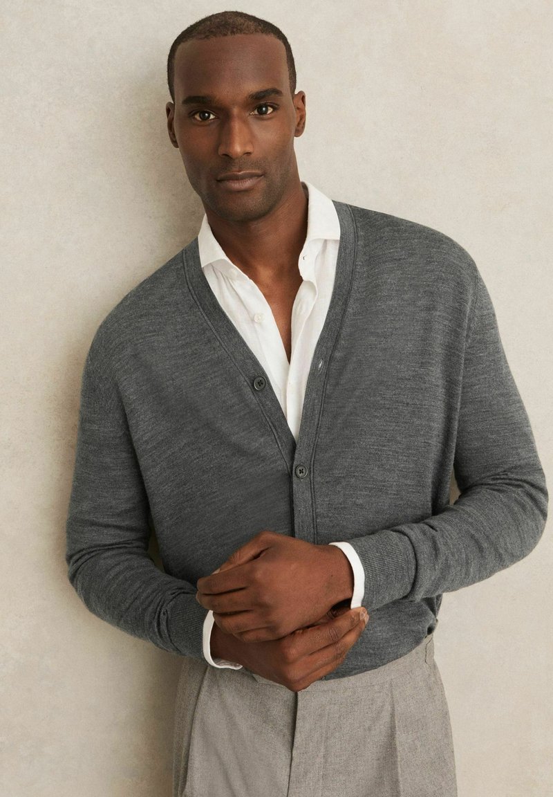 Gray knitted cardigan with a V-neck, ribbed cuffs, and three buttons, layered over a white shirt. The fabric appears soft and textured.