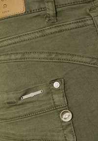 Olivgröna denimjeans med en mjuk textur, flera fickor, kontrasterande sömmar och en metallknapp med logotypdetalj.