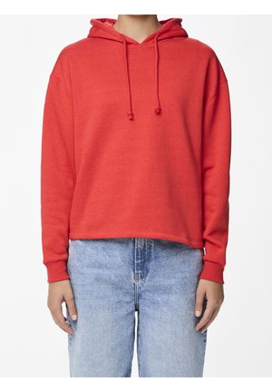 Osoba w prostym czerwonym kapturze z troczkami i jasnoniebieskich, wysokowzrostowych dżinsach, pokazana od ramion do bioder na białym tle.