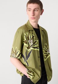 Rövid ujjú, zöld ing, könnyű anyagból készült, nagy sárga és fekete virágmintákkal, laza szabású, gombos záródással.