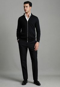 Maglione nero con zip e colletto bianco, indossato sopra una camicia bianca. Abbinato a pantaloni neri e scarpe lucide nere. Tessuto liscio.