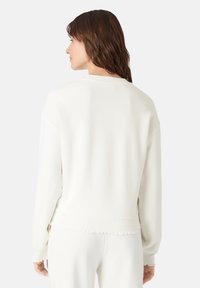 Felpa bianca con scollatura rotonda, spalle scese e polsini a coste. Presenta un orlo sfrangiato per un tocco di texture.