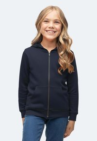 Felpa con zip di colore blu navy realizzata in materiale morbido, con cappuccio, tasche frontali e polsini a costine. Abbinata a jeans blu.