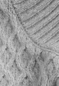 Hellgrauer Strickstoff, der ein strukturiertes Muster mit diagonalen und diamantförmigen Formen sowie weichen, flauschigen Fasern zeigt.