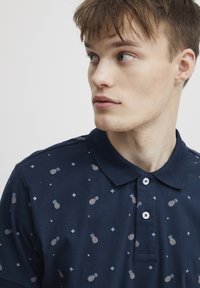 Polo majica temno modre barve iz bombaža, s patternom ananasa in diamanta, z ovratnikom in zapenjanjem na dva gumba.