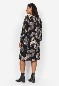 Svart klänning med ett abstrakt leopardmönster i beige och ljusgrått, med långa ärmar och en avspänd passform, kombinerad med svarta ankelstövlar.