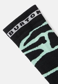 Ciorap negru cu un model abstract verde mentă, având o textură tricotată și o bandă albă cu logo-ul "BURTON" în partea de sus.