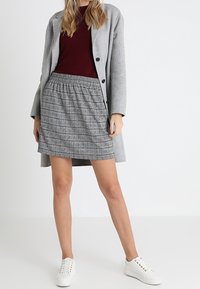 Abrigo de lana gris con botones negros sobre un suéter burdeos y una falda texturizada gris con rayas horizontales; combinado con zapatillas blancas.