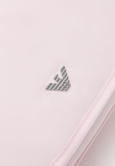 Light pink fabric features a silver winged logo with geometric patterns. The detailed zipper edge highlights the design.