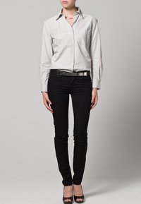 Ljusgrå skjorta med knappar, svarta skinny jeans, svart bälte med metallackent, och svarta öppna klackskor. Slät tyg med skräddarsydd passform.