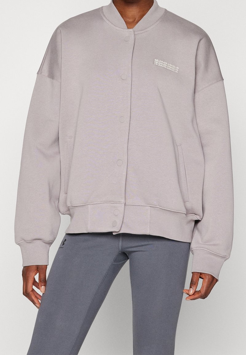 Chaqueta de sudadera gris claro con cierre de botones, dobladillo acanalado y ajuste holgado. Presenta un sutil detalle del logo en el pecho y bolsillos laterales.