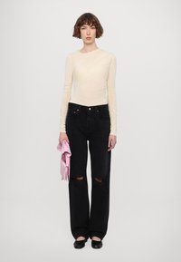 Light cream long-sleeve top with textured fabric, paired with black wide-leg jeans featuring distressed knees, and holding a pink garment.
