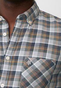 Karierte Hemd mit Button-Down-Kragen, in Grautönen, Grün und Orange, aus Baumwollstoff, Tasche mit besticktem Logo und weißen Knöpfen.