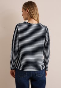 Marineblau-weiß gestreiftes Langarmoberteil mit Rundhalsausschnitt und geradem Schnitt. Getragen mit blauen Jeans, Rückansicht und Ärmel sichtbar.