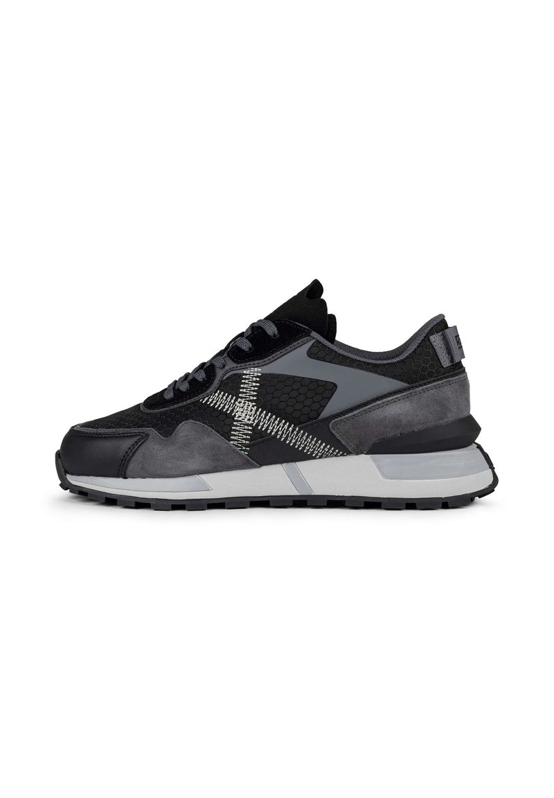 Basket de sport noire et grise avec des panneaux texturés, coutures blanches en zigzag, laçage à l’avant et semelle épaisse blanche et noire.