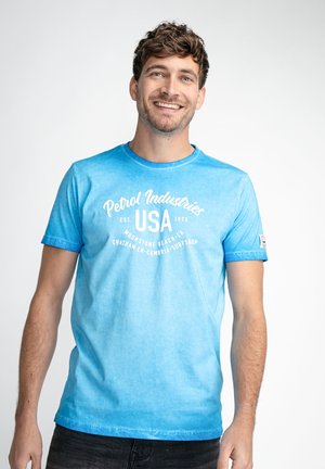 Camiseta de algodón azul con un estampado gráfico blanco que lleva el texto "Petrol Industries USA", mangas cortas y cuello redondo.