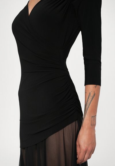 Rochie lungă neagră cu mâneci lungi, decolteu în V și detalii plisate în talie. Material moale cu o textură netedă și fustă din material transparent stratificat.