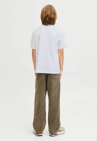 Valge lühikeste varrukatega T-särk, mille juurde on sobitatud hallid ja rohelised laiad püksid. Püksid on tekstuuriga viimistlusega ja neil on tagakotid. Kingad on hallid ja valged.