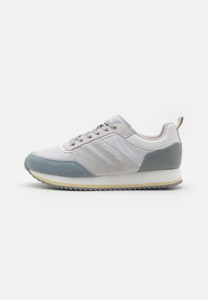 Sneaker grigio chiaro e blu con una superficie liscia e scamosciata, caratterizzato da una punta arrotondata, chiusura con lacci e una suola in gomma rigata.