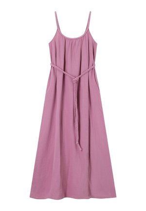 Femme aux longs cheveux bruns portant une robe rose sans manches ainsi que des colliers et bracelets colorés en perles sur un fond neutre.