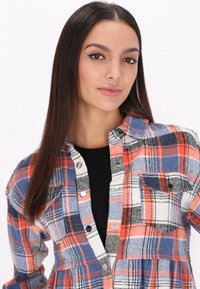 Plaid button-up shirt in orange, blue, and white. Features two front pockets, silver hardware, and a relaxed fit design.