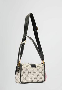 Biela crossbody taška s vzorom a čiernymi akcentmi, s prepracovaným tvarom, nastaviteľným popruhom a detailmi zlatého kovu.
