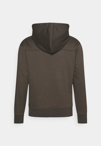 Sudadera con capucha marrón, que presenta mangas largas, costuras planas y un tejido texturizado. La capucha se sitúa alta, integrándose en el diseño trasero.