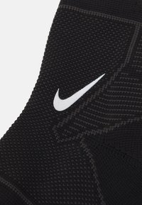 Fekete Nike zokni, textúrált kötött anyagból, szoros fazonnal és egy markáns fehér swoosh logóval a külső oldalán.