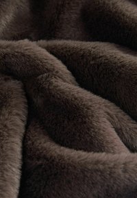 Țesătură din blană artificială maro cu o textură moale și densă, având un model ondulat și o strălucire subtilă, creând un aspect plăcut la atingere.