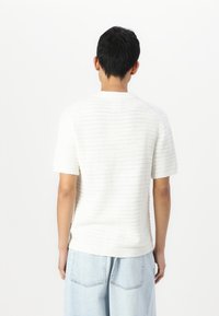 Suéter blanco de punto con mangas cortas, patrón texturizado, y cuello y dobladillo acanalados. Combinado con jeans de pierna ancha en azul claro.