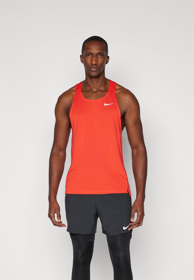 Top deportivo rojo de Nike con una textura transpirable, que presenta un escote redondo, tirantes anchos y un pequeño logo blanco en el pecho. Pantalones cortos negros debajo.