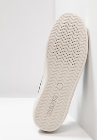 Biała gumowa podeszwa zewnętrzna z zygzakowatym wzorem i otworami wentylacyjnymi. Marka „GEOX” wytłoczona w pobliżu środka. Zakrzywione, gładkie krawędzie.