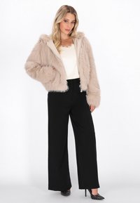 Beige nep bont, verkorte jas met een capuchon, ritssluiting en tekstuur mouwen, gecombineerd met zwarte wijde broek en studschoenen.